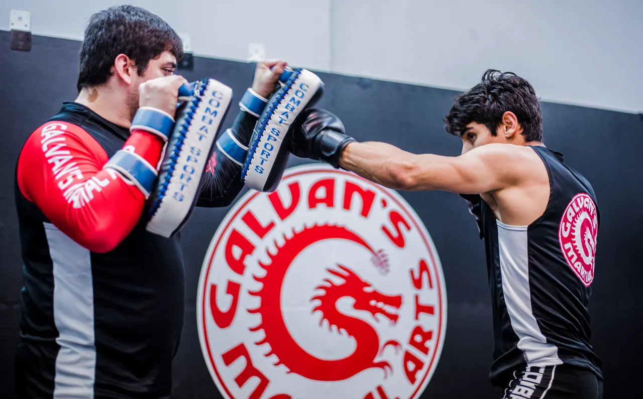 Un entrenador sostiene las manoplas mientras un alumno lanza un golpe recto durante una clase de kickboxing para adultos en Galvan's Martial Arts en Brownsville